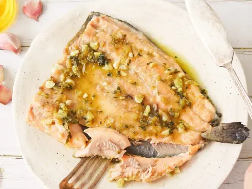 Deliciosa trucha al ajillo servida en un plato, con ajos y aceite de oliva alrededor.