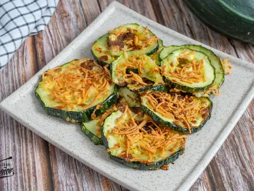 Rodajas de calabacín en freidora de aire, doradas y crujientes, con un toque de queso rallado. ¡Un snack saludable y delicioso!