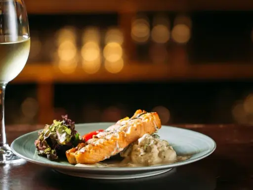 Un filete de salmón a la parrilla con ensalada y una copa de vino blanco, perfecto para un maridaje con riesling.