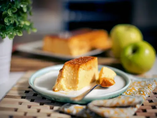 Un delicioso flan de manzana, con una porción servida en un plato, acompañado de manzanas verdes y una planta decorativa.