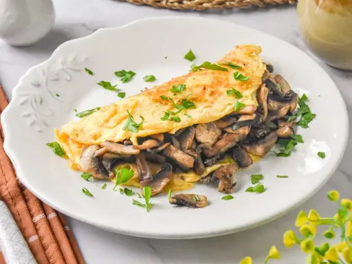 Tortilla de champiñones, dorada y esponjosa, rellena de sabrosos champiñones salteados y espolvoreada con perejil fresco.