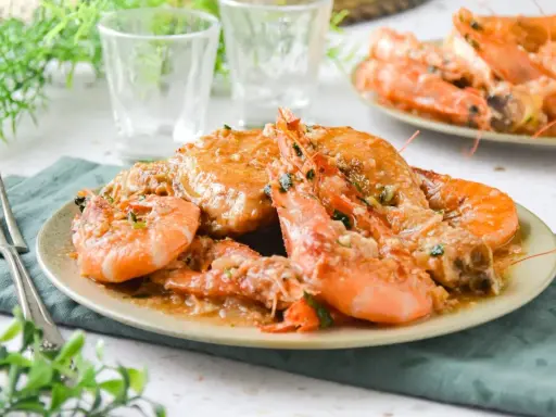Plato de pollo con gambas en salsa, decorado con perejil picado. Se ve delicioso y listo para disfrutar.