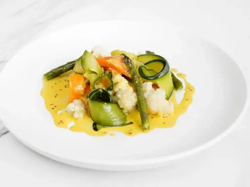 Deliciosas verduras al vapor, como zanahoria, calabacín en espiral, espárragos y coliflor, bañadas en una cremosa salsa amarilla.