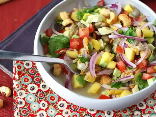 Un refrescante ceviche de berberechos con trozos de mango, aguacate, tomate y cebolla morada, servido en un cuenco blanco.