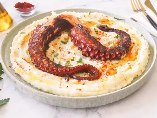 Delicioso pulpo a la brasa sobre puré de patatas cremoso, espolvoreado con pimentón y perejil.