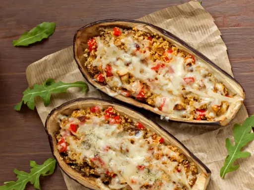 Dos mitades de berenjenas rellenas con cuscús, pimientos y queso derretido, cocinadas en airfryer.