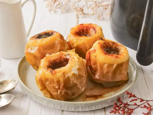 Cuatro manzanas asadas en freidora de aire, doradas y jugosas, con un relleno oscuro y especiado.