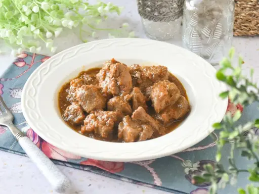 Plato de tierna carne de cerdo en salsa, servido en un cuenco blanco con un tenedor y decoración floral.