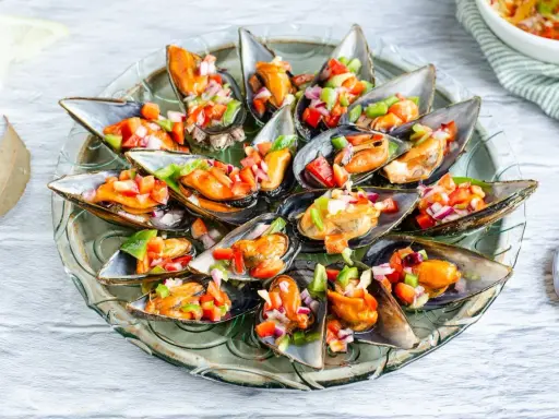 Mejillones a la vinagreta servidos en una bandeja de cristal, adornados con una colorida mezcla de pimientos y cebolla.