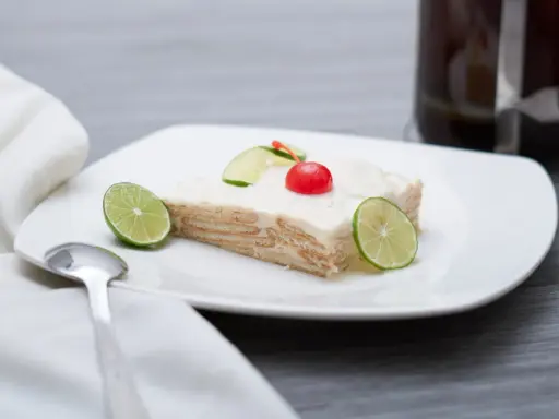 Deliciosa carlota de limón, con galletas y crema, decorada con rodajas de lima y una cereza.