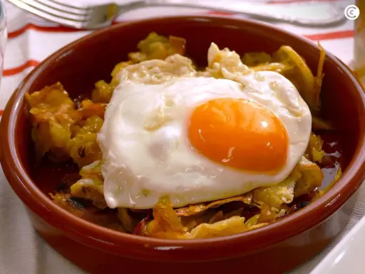 Un plato de patatas fritas con pimientos y un huevo estrellado encima, listo para disfrutar.