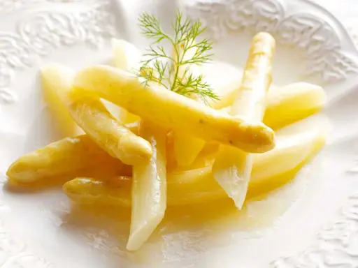 Espárragos blancos tiernos, listos para cocinar, servidos en un plato blanco con una ramita de eneldo.