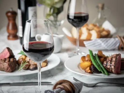 Dos copas de vino tinto, filetes jugosos y patatas asadas, perfectos para una cena de vino de invierno.