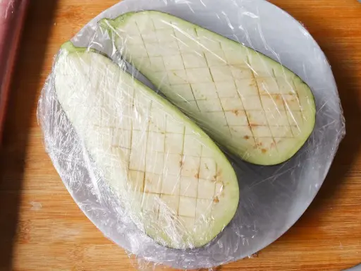 Dos mitades de berenjena cortadas en cubos y cubiertas con plástico, listas para cocinar berenjenas al microondas.