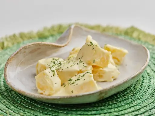 Patatas alioli cremosas y deliciosas, cubiertas con perejil fresco picado, servidas en un cuenco rústico sobre un salvamanteles verde.