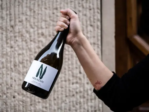 Mano sujeta botella de txakoli tinto Nekazari, con etiqueta blanca y letra "N" verde.