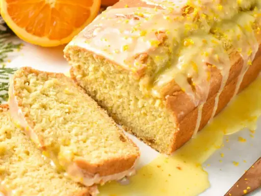 Un delicioso bizcocho de naranja, cubierto con glaseado y ralladura, con dos rebanadas cortadas.