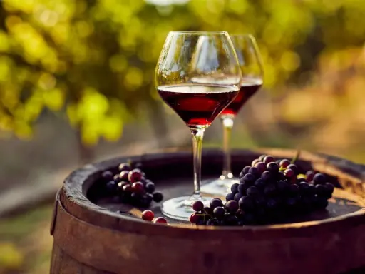Dos copas de vino tinto y racimos de uvas sobre un barril de madera, evocando las mejores añadas de Ribera del Duero.