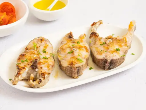 Tres rodajas de mero a la plancha, doradas y con perejil picado, servidas en plato blanco.