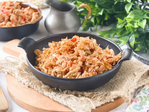 Delicioso pollo mechado con pimientos rojos y cebolla, servido en un cuenco negro sobre arpillera.