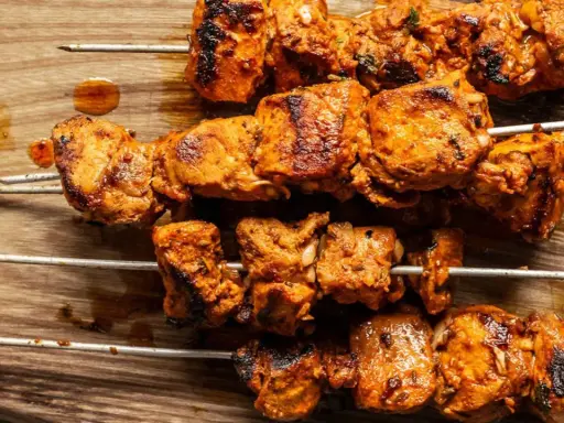 Cuatro brochetas de pinchos morunos auténticos, jugosos y dorados, sobre una tabla de madera.