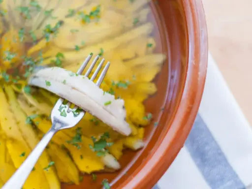 Boquerones en vinagre, la receta de la abuela, listos para disfrutar. Un tenedor recoge un boquerón marinado en aceite y vinagre, espolvoreado con perejil.