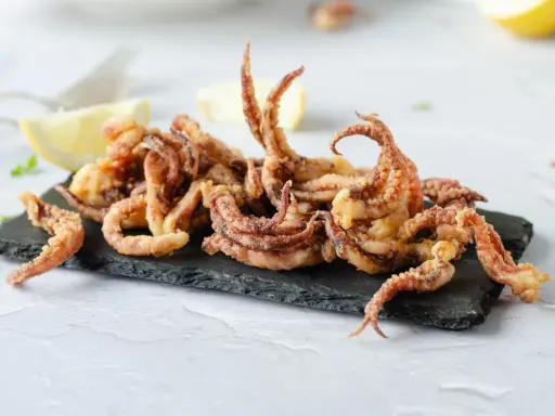 Crujientes rejos fritos servidos sobre pizarra negra, acompañados de gajos de limón.