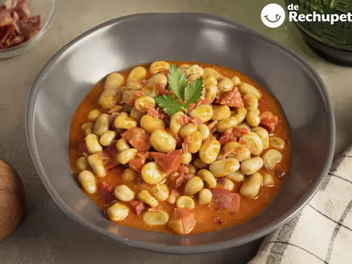 Plato de habas con jamón, guisadas en una salsa rojiza y decoradas con perejil.