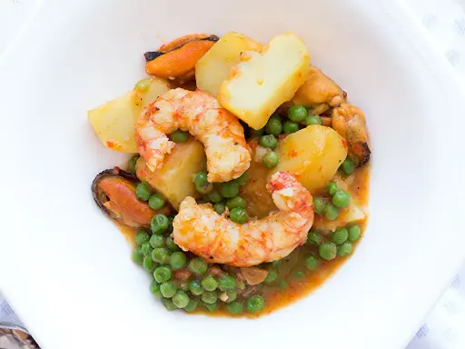 Patatas a la marinera con gambas, mejillones y guisantes en una salsa sabrosa.