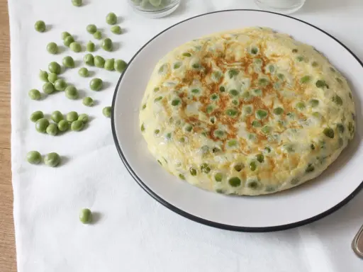 Tortilla de guisantes recién hecha, dorada y esponjosa, con guisantes verdes esparcidos por encima.