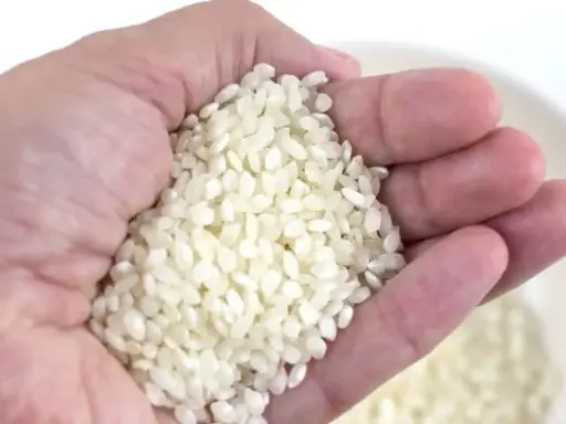 Mano sosteniendo arroz, una medida aproximada de cuanto arroz por persona para una comida deliciosa.