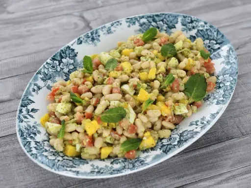 Deliciosa ensalada de alubias con trozos de tomate, mango y huevo, decorada con hojas de menta fresca.
