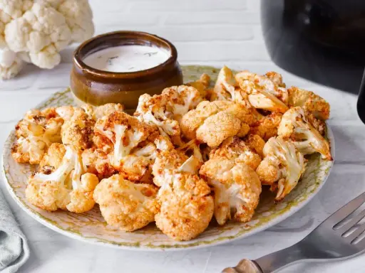 Coliflor airfryer dorada y crujiente servida en un plato con un tazón de salsa.