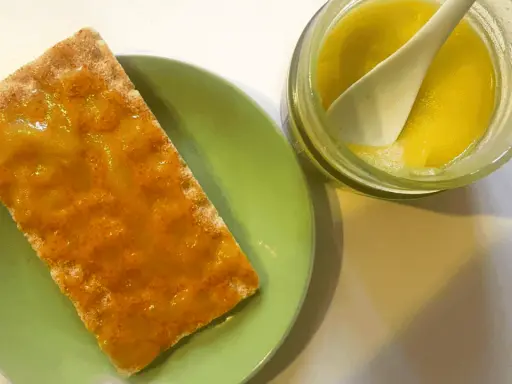 Galleta con mermelada de aceite de oliva, servida en plato verde junto a un tarro con la mermelada y una cuchara.