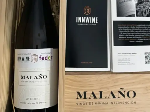 Caja de vino "Malaño" con etiqueta "Vino Solidario" y logos de INNWINE y feder. Incluye folleto informativo.