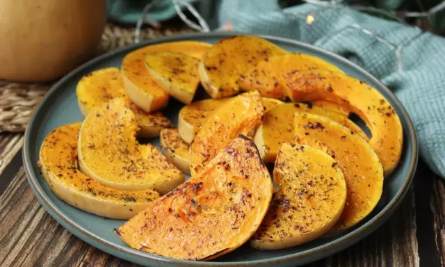Rodajas de calabaza a la plancha, doradas y sazonadas con hierbas, servidas en un plato azul.