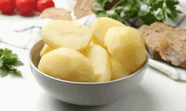 Un tazón lleno de patatas recién cocidas, listas para acompañar un pan rústico y tomates.