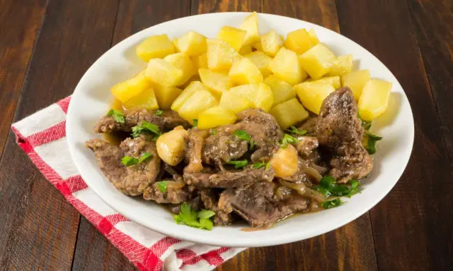 Plato de higaditos de pollo en salsa con patatas fritas en cubos, decorado con perejil fresco.