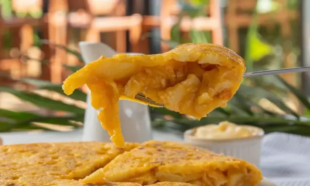 Un tenedor levanta un trozo de tortilla de patatas jugosa, mostrando su interior tierno y dorado.