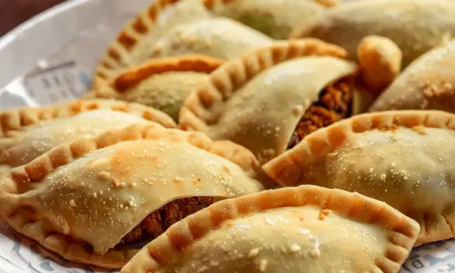 Empanadas doradas y crujientes, algunas con relleno visible de pechuga empanada, espolvoreadas con algo de sal.