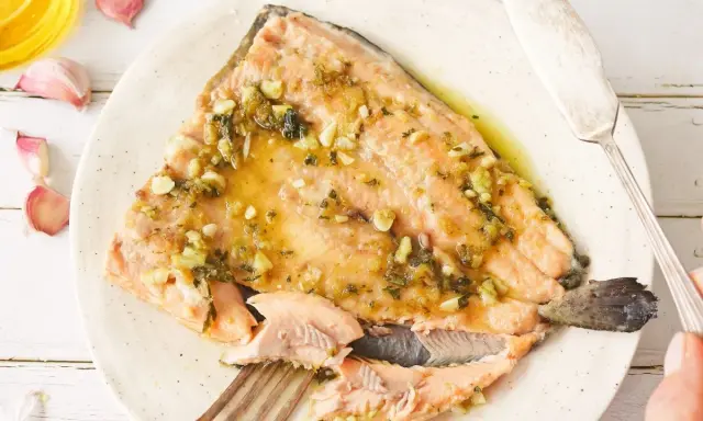 Deliciosa trucha al ajillo servida en un plato, con ajos y aceite de oliva alrededor.