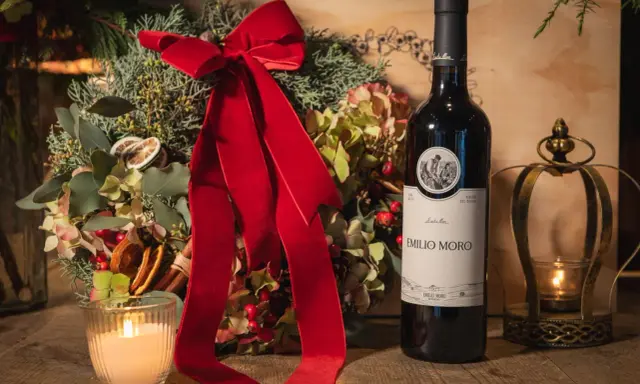 Botella de vino tinto fino Emilio Moro junto a un arreglo floral navideño, vela encendida y un candelabro dorado.