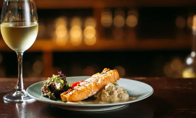 Un filete de salmón a la parrilla con ensalada y una copa de vino blanco, perfecto para un maridaje con riesling.
