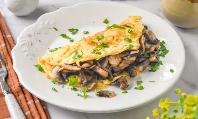 Tortilla de champiñones, dorada y esponjosa, rellena de sabrosos champiñones salteados y espolvoreada con perejil fresco.