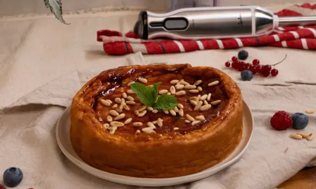 Bizcocho de avena casero, glaseado y decorado con piñones y menta. Frutos rojos y batidora al fondo.
