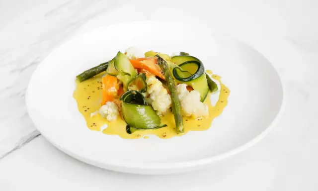 Deliciosas verduras al vapor, como zanahoria, calabacín en espiral, espárragos y coliflor, bañadas en una cremosa salsa amarilla.