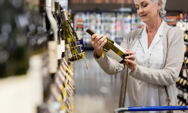 Mujer mayor elige una botella de vino español en el supermercado.