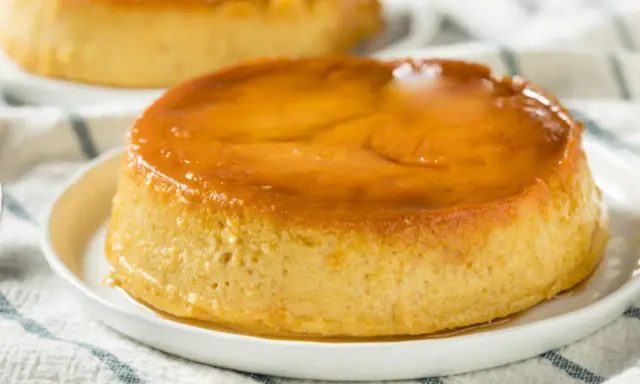 Delicioso flan de plátano con caramelo dorado, servido en un plato blanco sobre un mantel a rayas.