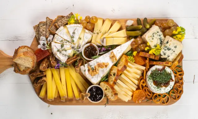 Una tabla de quesos sencilla con variedad de quesos, pan, frutas secas, uvas, pepinillos y mermelada.