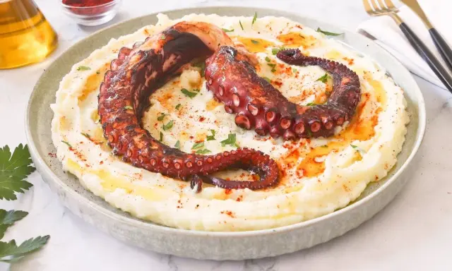 Delicioso pulpo a la brasa sobre puré de patatas cremoso, espolvoreado con pimentón y perejil.